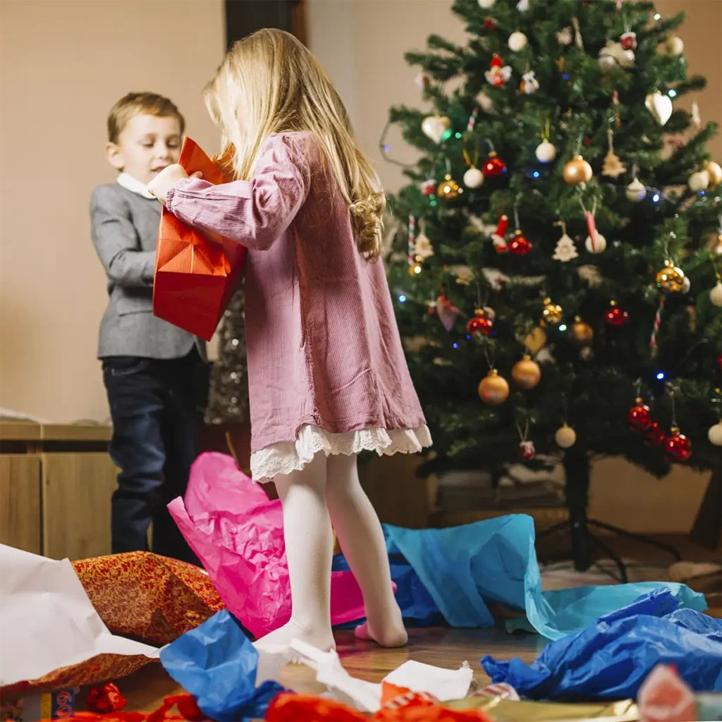 niños frente al árbol de navidad con muchos papeles de regalo en el suelo